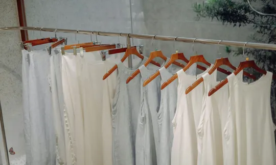 Vestidos de linho brancos e cinza-claro pendurados em cabides de madeira
